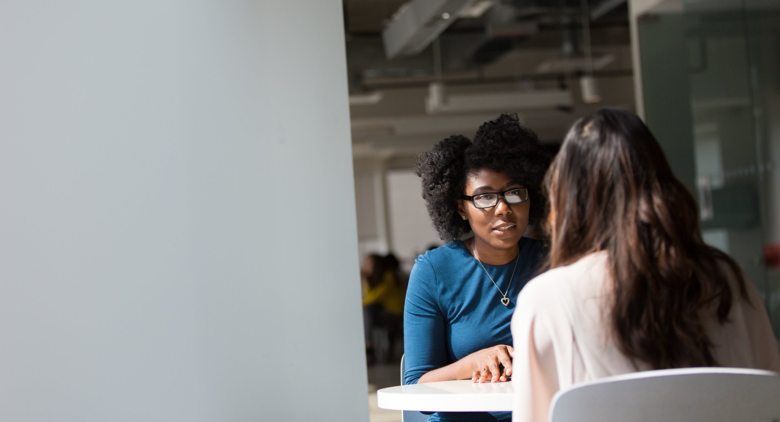 Woman at table speaking with another woman.