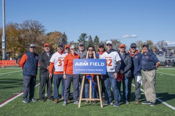 Members of ABM and Utica University stand on the football field by a sign that says 