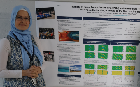 Hava Turkakin stands near a poster and looks at the camera.